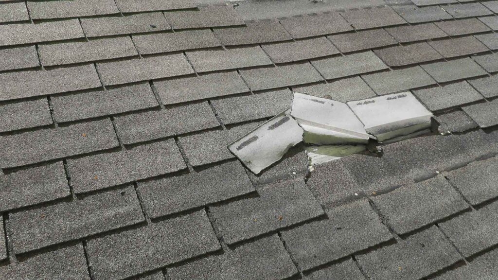Close-up of cracked shingles and damaged flashing on a residential roof